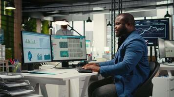 svart anställd använder sig av data och teknologi för företag förvaltning, granskning påstående grafer på övervaka till skapa rapporter och förbättra effektivitet, mål prestation. syn. kamera a. video