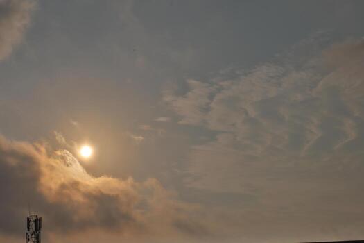 Sun shining through scattered clouds in a sky transitioning from orange to gray, nature photo