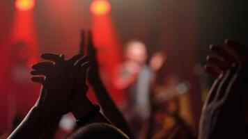 Enthusiastic crowd clapping hands at a live concert, illuminated by vibrant red lights, creating an energetic atmosphere video