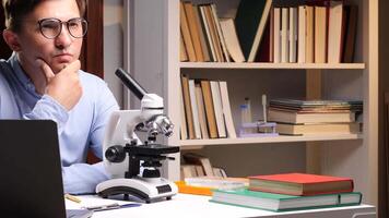 scientifique en pensant et travail à laboratoire bureau avec microscope et portable video