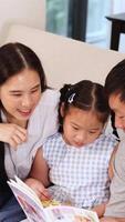 un' famiglia gode lettura un' libro insieme su un' divano, la creazione di un' caldo e coinvolgente atmosfera video