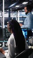 verticale Admin nel dati centro indossare cuffia assistere utenti con artificiale intelligenza risoluzione dei problemi. africano americano donna nel server camera centro gestione supporto Biglietti utilizzando automatizzato sistemi, telecamera un' video