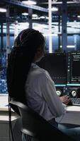 vertical dados Centro sistema administrador trabalhando em neural rede Programas desenvolvimento. africano americano mulher dentro servidor quarto implementando máquina Aprendendo tecnologia usando pc, Câmera uma video