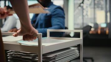 Close up of assistant pushing trolley cart with documents and folders from archive, bringing files to a colleague and ensuring efficient distribution of resources. Administrative tasks. Camera A. video