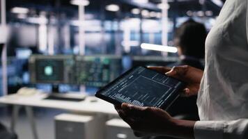 stänga upp av data Centrum programmerare använder sig av läsplatta, skrivning koda för resurs optimering, utför uppdateringar. server rum anställd använder sig av enhet, sammanställer programvara plåster till fixera buggar, kamera en video