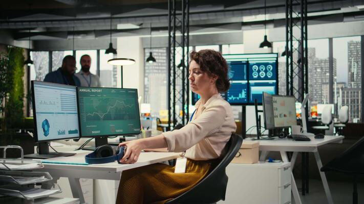 Office administrator uses focus music on headset to solve tasks, monitoring performance metrics at the workstation. Administrative tasks to ensure enterprise productivity and success. Camera A.