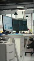 Vertical Empty business workplace filled with desks and dual monitors, modern and digital equipment to ensure multinational company success and efficiency. Office used for forecasting and report writing. video