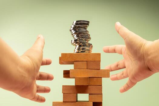 Coin Stack on precariously Jenga blocks, hands protecting it, symbolizing fragile financial stability and economic uncertainty, need for caution photo