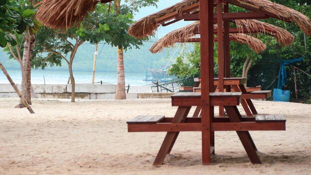 A thatched-roof hut with a picnic table sits on the beach, offering a cozy spot for tourists to rest and enjoy the view photo