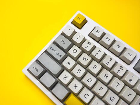 White mechanical keyboard with bright Esc key on bright yellow background, minimalism, keyboard buttons. A keyboard with a yellow key on the bottom left photo