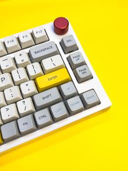 White mechanical keyboard with bright Enter key on bright yellow background, minimalism, vertical photo