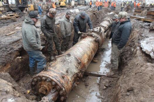 A group of men standing around a pipe in the mud photo