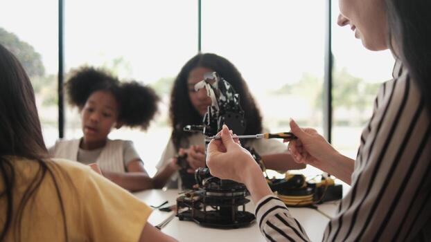 grupo de estudiante muchachas robótico brazos diseño y experimentar con hembra profesor instruyendo a aprendizaje mesa en primario Ciencias aula, que se discute tecnología conocimiento para niños de elemental escuela. foto