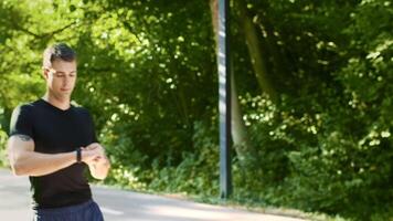 A young man jogs along a park pathway surrounded by lush greenery. He enjoys a summer day while focusing on maintaining a healthy lifestyle and fitness routine. video