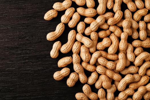 Unshelled peanuts spread across dark wooden surface showing natural texture and warm earthy tones in rustic setting photo