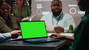 Diverse project staff working at night in office with chroma key on laptop, collaborating on reporting and setting business goals during a night time meeting in a corporation space. Camera B. video