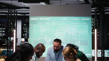 Coworkers prepare for a presentation by reviewing documents inside the strategy room at night, exchanging reports files and delivering forecasting updates for enterprise management. Camera A. video