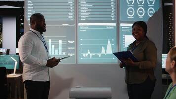 Black business advisors revealing monthly data insights during after hours briefing session, going into financial details and updates with the executive board members in dark office. Camera A. video