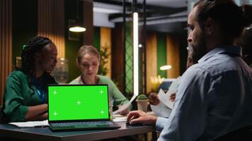 Diverse project team meeting after hours next to mockup display, sharing data visualization reports to discuss business intel. Forecasts for upcoming presentation to investors group. Camera A. video