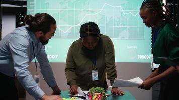 multi-etnisch experts vergadering naar bespreken gegevens voorspellingen na uren in briefing sessie, uitwisselen diagrammen bestanden en herzien budgettering updates. uitlijnen doelstellingen voor productiviteit. camera a. video