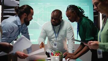 Diverse project team meeting after hours to share data visualization reports, discuss business intel and prepare forecasts for upcoming presentations to enterprise shareholders after hours. Camera A. video