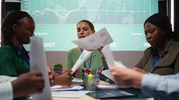Close up of diverse staff hand over data projections papers in a meeting after hours for multinational company operations. Risk assessment and visual data to support forecasting. Camera A. video