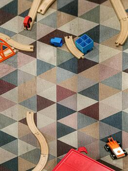 This overhead shot presents a playful scene with wooden toy train tracks and colorful blocks arranged on a floor featuring a geometric triangle pattern. Geometric play. photo