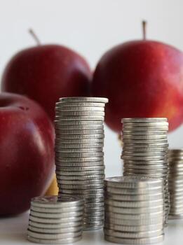 Concept photo of fruits cost. Three red apples and columns of coins closeup stock photo