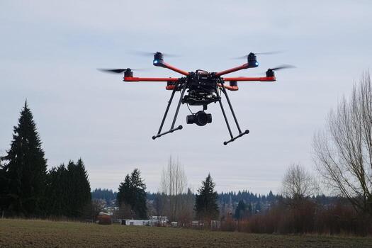 A large black and red drone flying over a field photo