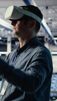 Vertical Data center system administrator uses virtual reality tech, improving AI rigs processing speed. Man in server farm wearing VR goggles to provide support for artificial intelligence workloads, camera B video