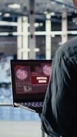 Vertical Engineer in server room receives critical error popup on laptop screen, dealing with urgent system issues. Data center worker gets notification about hardware problems affecting performance, camera B video