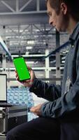 vertikal server rum programvara utvecklare använder sig av attrapp telefon medan väntar för uppdateringar till Avsluta installerar. data Centrum ingenjör användningar grön skärm smartphone, väntar för koda till Avsluta sammanställa, kamera en video