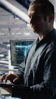 Vertical Data center technician monitors deep learning process with laptop, reviewing operational metrics. IT expert reviews neural networks reports during inspection to verify ongoing stability video