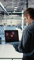 Vertical Engineer in server room receives critical error popup on laptop screen, dealing with urgent system issues. Data center worker gets notification about hardware problems affecting performance, camera A video
