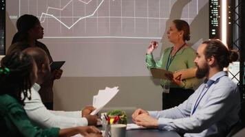 multietnisk experter team utvärdera data prestanda metrik på utsprång styrelse, granskning data insikter med investerare grupp i verkställande session efter timmar. företags- händelse på natt. kamera b. video