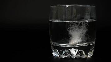 en närbild av ett bubblande läsplatta upplösande i en glas av vatten på en svart bakgrund. de gnistrande verkan skapar bubblor och en molnig flytande. de fokus är på de surfplattans reaktion. video