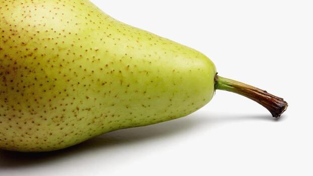 A light green pear with brown dots and a petiole lies on a white surface. Its fresh look is ideal for culinary and natural projects. photo
