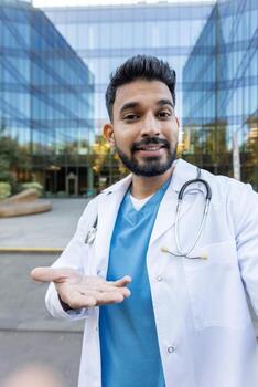 A friendly doctor in a call using a phone app, presenting a modern clinic in the background, smiling at the camera photo