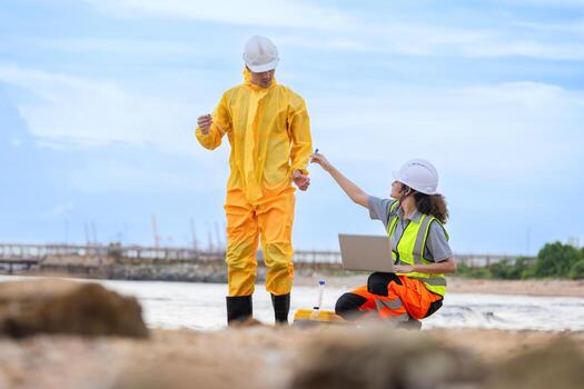 Environmental Scientists Collecting Water Samples for Analysis, Researchers in Protective Gear Studying Water Quality at Site, Ecologists Working on Beach, Monitoring Environmental Contamination photo