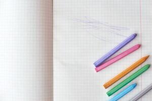 Colorful crayons lined up on opened graph paper notebook with abstract scribbles. photo