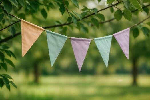 Orange, green and purple fabric triangle flags hanging on tree branch against blurred green background. Outdoor decoration photography with shallow depth of field. Party decoration concept. photo