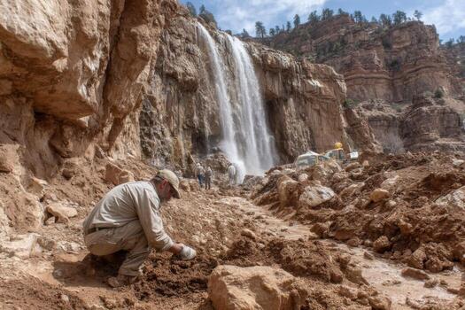 A man is digging dirt in front of a waterfall photo