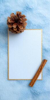 Elegant flat lay of blank postcard with golden edges and pine cone on textured blue background photo