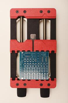 Stable universal holder designed for circuit boards, featuring a bright red example PCB in its grasp. photo