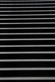 Image shows a series of evenly spaced horizontal metal bars against a dark background, creating a repetitive linear pattern. Suitable for illustrating concepts of structure, security, or industrial design in visual projects. photo
