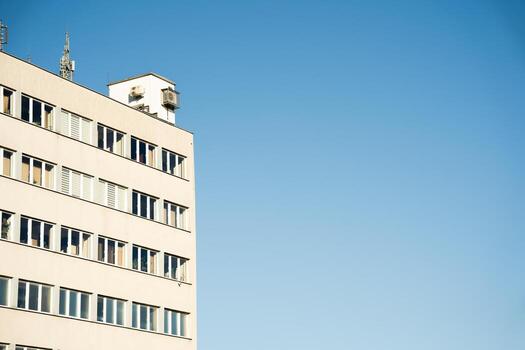 Rectangular office building with multiple windows and rooftop equipment, set against a clear blue sky. Suitable for illustrating urban architecture, business environments, or city infrastructure concepts. photo