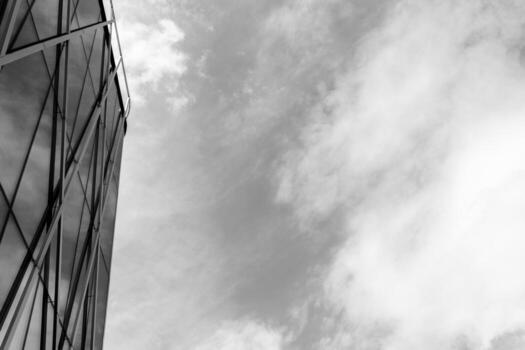 A contemporary glass building with geometric metal framework is shown on the left, contrasted by a cloudy sky on the right. Suitable for illustrating urban architecture, modern design, or cityscape concepts in editorial or commercial projects. photo