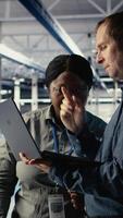 Vertical Team of data center engineers investigate neural networks configuration, making adjustments. Teamworking server hub coworkers use notebook to check deep learning errors, camera A video