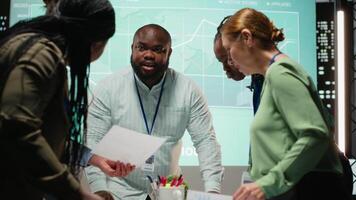 nacht tijd vergadering ontvouwt zich net zo een multi-etnisch team verzamelt in een strategie kamer, analyseren zichtbaar gegevens, statistieken en risico beoordeling bestanden naar rit project ontwikkeling voor efficiëntie. camera b. video