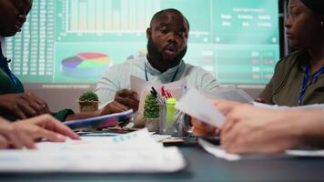 multietnisk team granskning infographics till erbjudande lösningar till fixera projekt frågor, arbetssätt efter timmar till Avsluta uppgifter innan deadline. analytiker delta problem lösning möte. kamera a. video